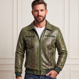 May include: A long-sleeve olive green jacket featuring a textured snakeskin pattern, a classic collar, a full-length front zipper, and two horizontal zippered chest pockets. The garment includes ribbed cuffs and a ribbed hem, worn over a white shirt.