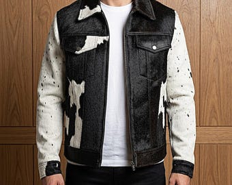 May include: A jacket featuring a black and white cowhide pattern on the torso and sleeves. The garment has a pointed collar, a full-length front zipper, two chest pockets with buttoned flaps, and buttoned cuffs, worn over a plain white t-shirt.