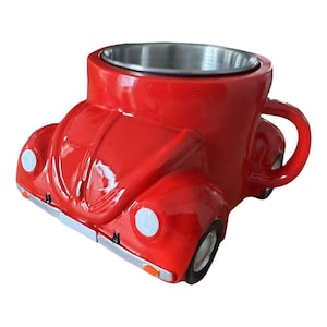 Puede incluir: Una taza de cerámica roja con forma de Volkswagen Beetle clásico. La taza tiene un interior de acero inoxidable y un asa en el lateral.