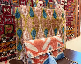 May include: A large tote bag and a small clutch, both with a patterned design in shades of brown, blue, and orange. The clutch has a blue tassel and a gold chain strap. The background features a patterned textile.
