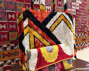 May include: A large tote bag and a small clutch with a colorful geometric pattern. The tote bag has a black, orange, yellow, and white design. The clutch is red, yellow, and pink with a tassel and chain strap.