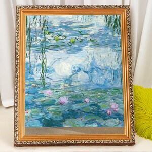 May include: A framed painting of a water lily pond with blue and green water, white clouds, and pink water lilies. The frame is gold with a decorative border.
