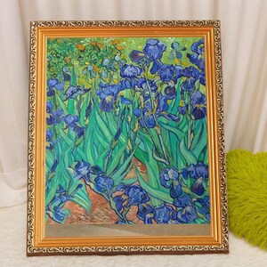 May include: A framed painting of a field of blue irises with green leaves. The painting is in a gold frame with a decorative border.