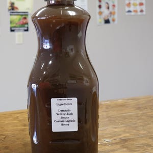 May include: A brown glass bottle with a black cap, labeled "Bathroom Detox" and listing ingredients: Damiana, Yellow dock, Senna, Cascara sagrada, Honey.