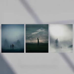 May include: Three framed art prints depicting surreal landscapes. The first shows two figures in a foggy environment. The second depicts a dark, vertical monolith in a field. The third shows a silhouetted figure in a misty setting.