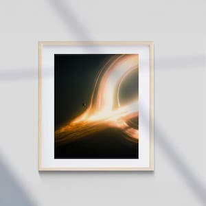 Peut inclure: Impression encadrée représentant un trou noir. L'œuvre d'art présente des bandes tourbillonnantes de lumière orange et jaune sur un fond sombre, avec une petite sphère sombre visible. Le cadre est en bois clair.