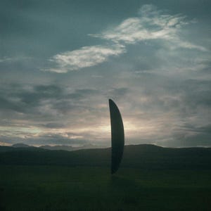 May include: A dark, curved, vertical object hovers over a green field, with hills and a cloudy sky in the background. The object's form resembles a blade or a crescent, with a dark, solid hue. The scene creates a sense of mystery and intrigue.