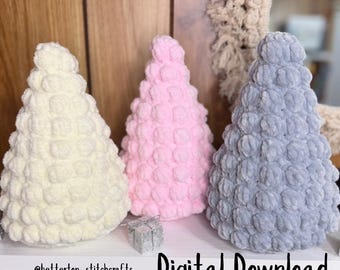 Könnte beinhalten: Drei gehäkelte Weihnachtsbäume in Creme, Rosa und Grau mit einer Noppenstichstruktur. Der Text "Bobble Christmas Tree Crochet Pattern" steht oben. Die Worte "Digital Download" stehen unten. Vor den Bäumen befindet sich eine kleine silberne Geschenkbox.