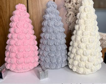 Könnte beinhalten: Drei handgefertigte gehäkelte Weihnachtsbäume in Rosa, Grau und Weiß. Die Bäume haben eine Noppenstich-Textur und werden auf einem weißen Regal ausgestellt. Der Text oben lautet "Tall Bobble Christmas Tree Crochet Pattern". Die Worte "Digital Download" sind ebenfalls sichtbar.
