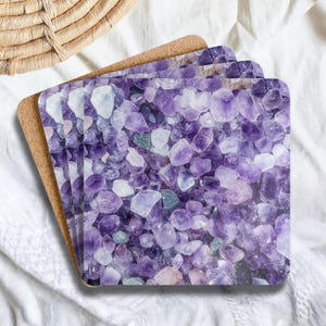 May include: A set of square coasters featuring a high-resolution print of raw amethyst crystals in various shades of purple, lavender, and white. Each coaster has a smooth top surface and a natural brown cork backing for a stable grip.