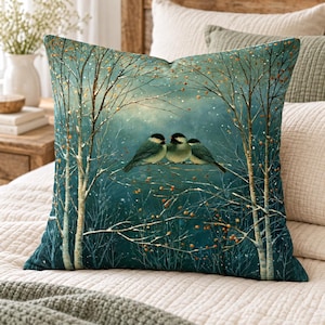 May include: A square throw pillow featuring a printed illustration of three small birds perched on a thin branch. The scene depicts a winter forest with teal and blue tones, bare white birch trees, and small orange berries against a snowy backdrop.