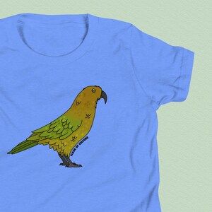 Op de afbeelding: Lichtblauw T-shirt met een cartoon illustratie van een geel en groene vogel. De vogel kijkt naar rechts. De tekst "FLASH OF CULTURE" staat verticaal aan de rechterkant van de vogel. Een casual top voor dagelijks gebruik.