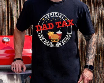 May include: Black t-shirt with a circular graphic that reads "OFFICIAL DAD TAX FOOD INSPECTION SERVICE" in white and red. The graphic includes a burger, fries, and a drink. The shirt is being worn.