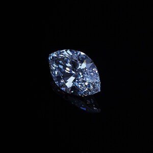 May include: A marquise-cut, light blue diamond against a black background. The diamond's facets reflect light, creating a sparkling effect. The gemstone is the focal point, with a dark, reflective surface beneath.