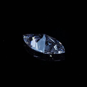 May include: A marquise-cut diamond, with a brilliant, multifaceted surface, is displayed against a stark black background. The gemstone's clear, icy facets reflect light, creating a dazzling display of brilliance and sparkle. The elongated shape is a classic choice for jewelry.