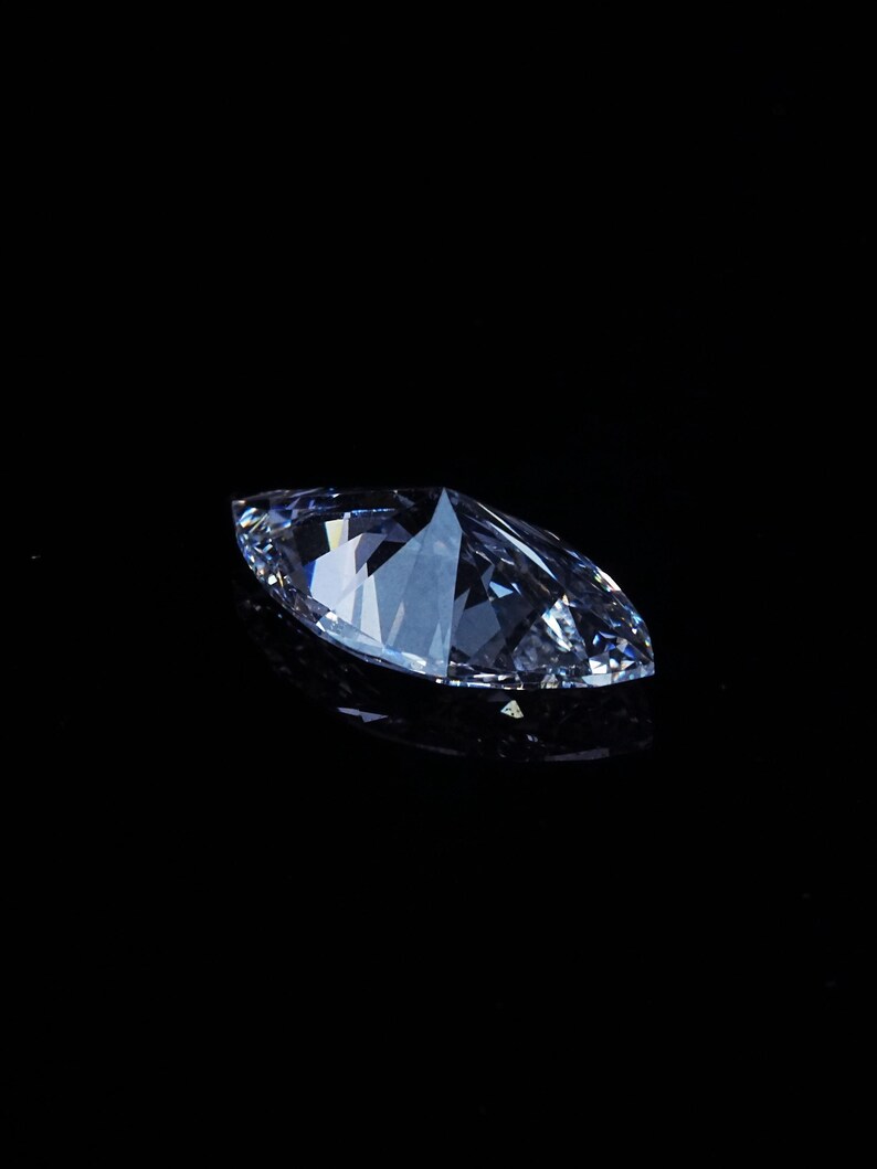May include: A marquise-cut diamond, with a brilliant, multifaceted surface, is displayed against a stark black background. The gemstone's clear, icy facets reflect light, creating a dazzling display of brilliance and sparkle. The elongated shape is a classic choice for jewelry.