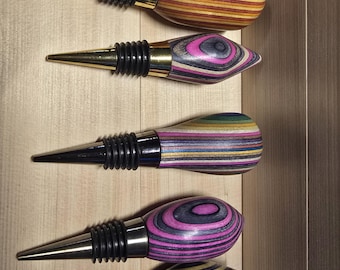 May include: Five wooden wine bottle stoppers with different colorful wood grain patterns and gold metal tops. The stoppers are arranged vertically in a row.