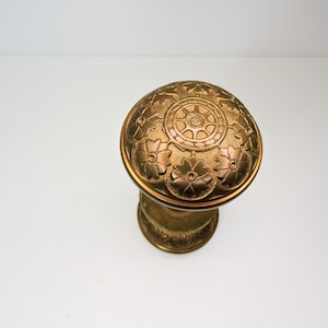 May include: A gold door knob with a decorative floral design and a central wheel-like pattern.