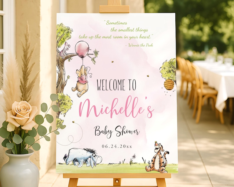 Editable baby shower welcome sign for a girl with pink text and soft watercolor illustrations of Winnie the Pooh holding a pink balloon, Piglet in a tree, Eeyore, and Tigger; printable sign displayed outdoors on a wooden easel.