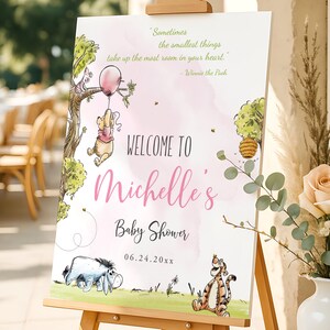 Girl baby shower welcome sign with Winnie the Pooh holding a pink balloon, Piglet in a tree, and Tigger and Eeyore on the grass; editable and printable design in soft pastel tones, displayed on an easel for outdoor decoration.