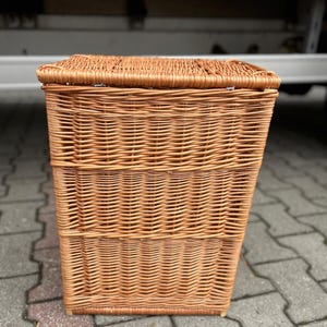 May include: A rectangular wicker basket with a lid, woven from light brown material. The basket has a textured surface and a fitted lid. It is designed for storage and measures approximately 40cm in height.