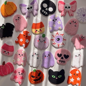 May include: A selection of colourful, textured Halloween decorations. The collection features pumpkins, ghosts, skulls, bats, candy corn, and a spiderweb, in shades of pink, orange, purple, and black. Each item has a unique design.