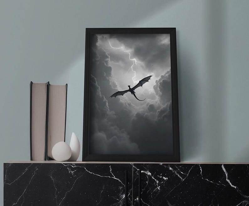 Op de afbeelding: Een zwart-wit ingelijste print van een silhouet van een draak die door een stormachtige lucht met bliksem vliegt.