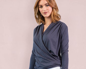 Puede incluir: Una blusa de manga larga en color gris carbón oscuro con frente estilo cruzado, escote en V y dobladillo fruncido, combinada con pantalones vaqueros blancos. La prenda está confeccionada en tela suave y lisa con un diseño drapeado y superpuesto.