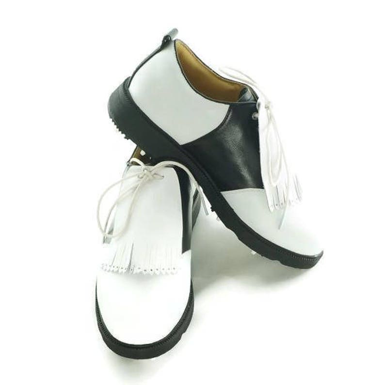 White leather golf shoe kilties on a pair of men's black and white saddle style golf shoes with white shoe laces and black soles. Kilties have 15 fringes each with a single perforation in the point. Front view.