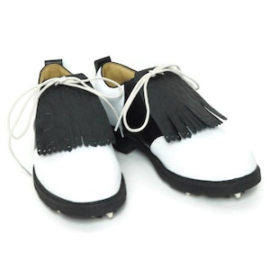 Black alligator embossed leather shoe fringes on a pair of black and white saddle shoes for men, tied with white shoe laces, black rubber soles. Classic kilties have 16 fringes with a single perforation near each tip. Front view.