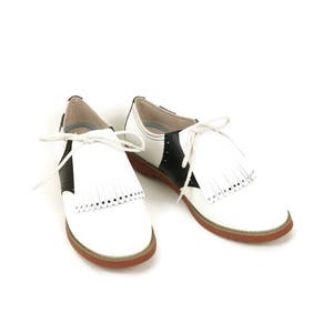 White leather shoe fringes laced on to a pair of womens saddle shoes.  These classic kilties have 14 individual fringes each with a small hole punched near the pointy tip