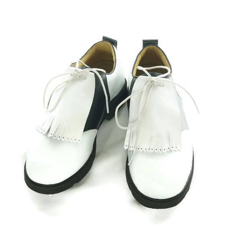 White leather golf shoe kilties on a pair of men's black and white saddle style golf shoes with white shoe laces and black soles. Kilties have 15 fringes each with a single perforation in the point. Front view.