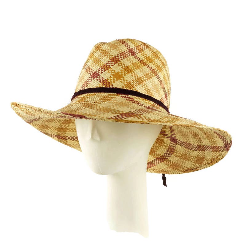 May include: A wide-brimmed straw hat with a checkered pattern in shades of brown and red. The hat has a brown ribbon around the crown.