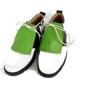 Lime green apple golf shoe kilties on a pair of mens black and white saddle style golf shoes with white shoe laces and black soles. Kilties have 15 fringes each with a single perforation in the point. Front view. White background.