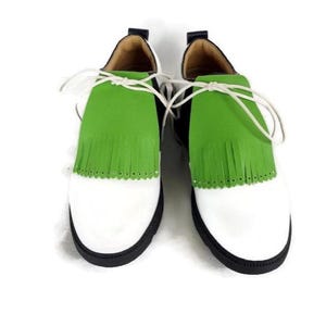 Lime green apple golf shoe kilties on a pair of mens black and white saddle style golf shoes with white shoe laces and black soles. Kilties have 15 fringes each with a single perforation in the point. Front view. White background.