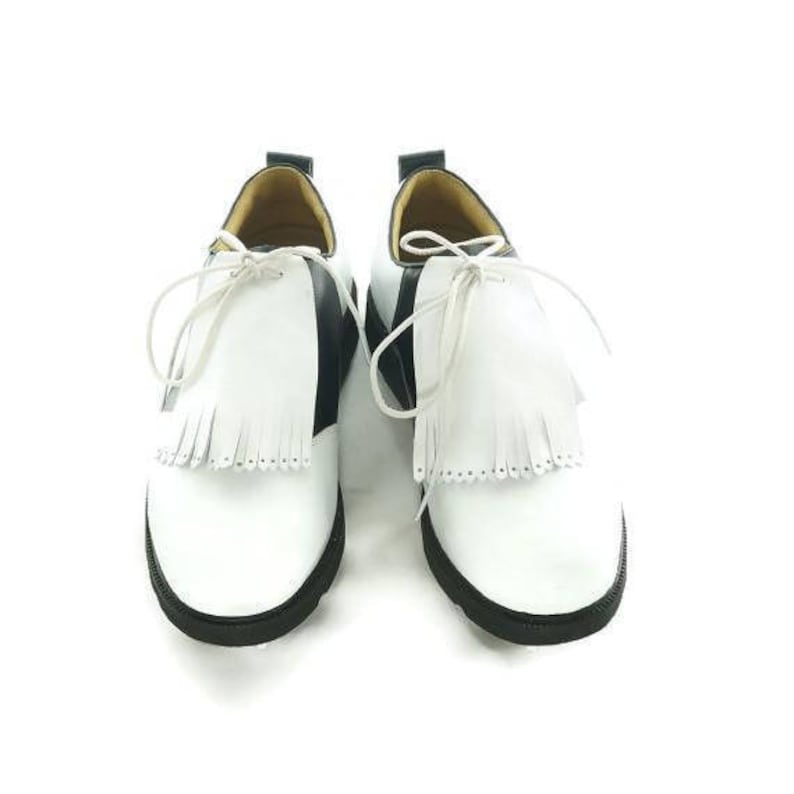 White leather golf shoe kilties on a pair of men's black and white saddle style golf shoes with white shoe laces and black soles. Kilties have 15 fringes each with a single perforation in the point. Front view.