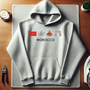 May include: A grey hoodie featuring a graphic of a Moroccan flag, a teapot, a tagine, and an archway. The text "MOROCCO" is printed below the graphic.