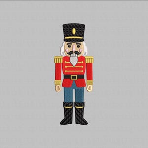 May include: Embroidered image of a toy soldier nutcracker. The nutcracker wears a black hat with a gold accent, a red jacket with gold epaulets, blue pants, and black boots. The nutcracker has a white beard and mustache.