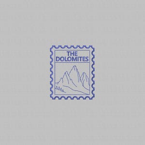 May include: A blue embroidered design on a light gray fabric background, shaped like a postage stamp with scalloped edges. The design features a mountain range outline and the text THE DOLOMITES centered within the rectangular border.
