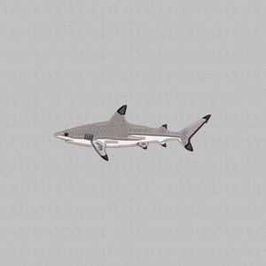 Puede incluir: Un parche bordado que muestra un tiburón gris con el vientre blanco y las puntas de las aletas negras. El tiburón se muestra de perfil, con costuras detalladas que definen sus branquias, el ojo y la forma aerodinámica de su cuerpo.