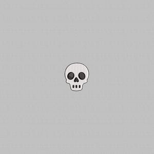 Puede incluir: Un pequeño parche bordado con forma de calavera, con contorno blanco y cuencas de los ojos y nariz negras. La calavera tiene tres pequeños puntos para la boca. El parche está centrado sobre un fondo gris claro.