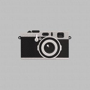 May include: Embroidered design of a vintage camera in black and silver. The camera features a prominent lens, buttons, and a flash. The design is set against a gray background, creating a classic and detailed aesthetic.