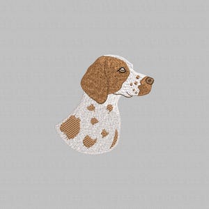 Puede incluir: Imagen bordada de la cabeza y el cuello de un perro, con una base blanca y manchas marrones y una oreja marrón. El perro mira hacia la derecha, con un ojo y una nariz detallados. El bordado tiene un aspecto texturizado, sobre un fondo gris.