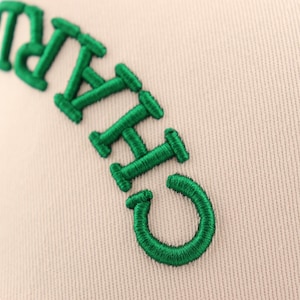 Op de afbeelding: Close-up van een beige baseballpet met groene geborduurde letters die "CHICAGO" lezen.