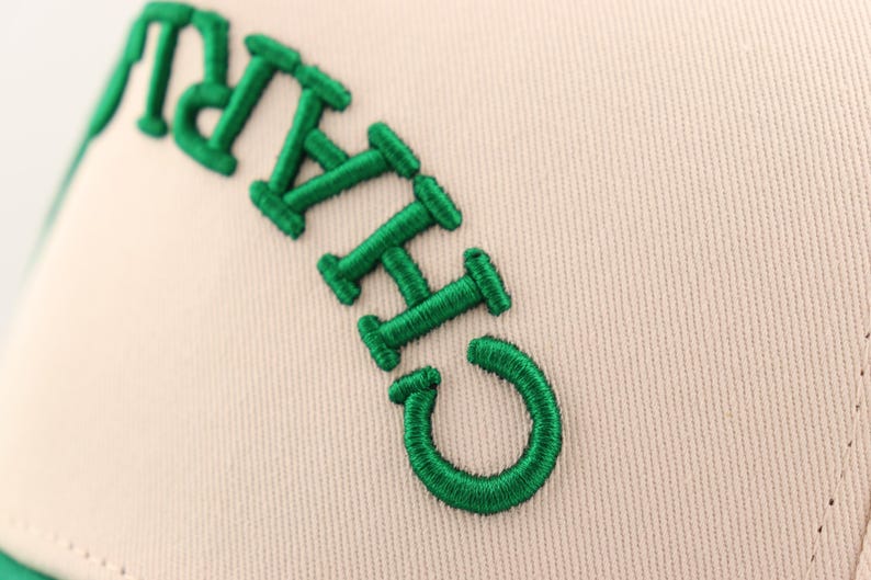 Op de afbeelding: Close-up van een beige baseballpet met groene geborduurde letters die "CHICAGO" lezen.