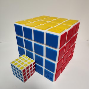 May include: A large, multi-colored Cube Jack puzzle next to a smaller version. The larger cube features yellow, blue, and red sides. The smaller cube has the same color scheme. The text "CUBE JACK" is visible on the larger cube.
