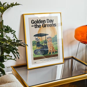 May include: A framed poster with a gold frame. The poster features a golden retriever dog sitting in a golf cart on a green golf course. The poster's title is "Golden Day on the Greens".