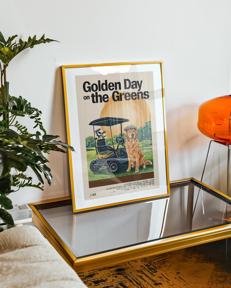 May include: A framed poster with a gold frame. The poster features a golden retriever dog sitting in a golf cart on a green golf course. The poster's title is "Golden Day on the Greens".