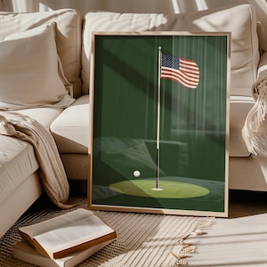 May include: A framed print of a golf green with a flagpole and an American flag waving in the wind. A white golf ball sits on the green.