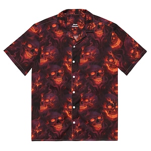 Puede incluir: Una camisa de manga corta con botones y estampado de calaveras y llamas. La camisa tiene un fondo oscuro con llamas rojas y naranjas y calaveras.